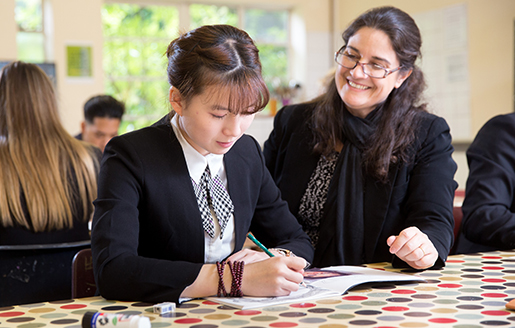 student writing in a book as a teacher looks on smiling