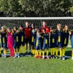 St. John’s Senior School football squad with their two coaches in a team photo on a sunny grass pitch