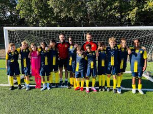 St. John’s Senior School football squad with their two coaches in a team photo on a sunny grass pitch