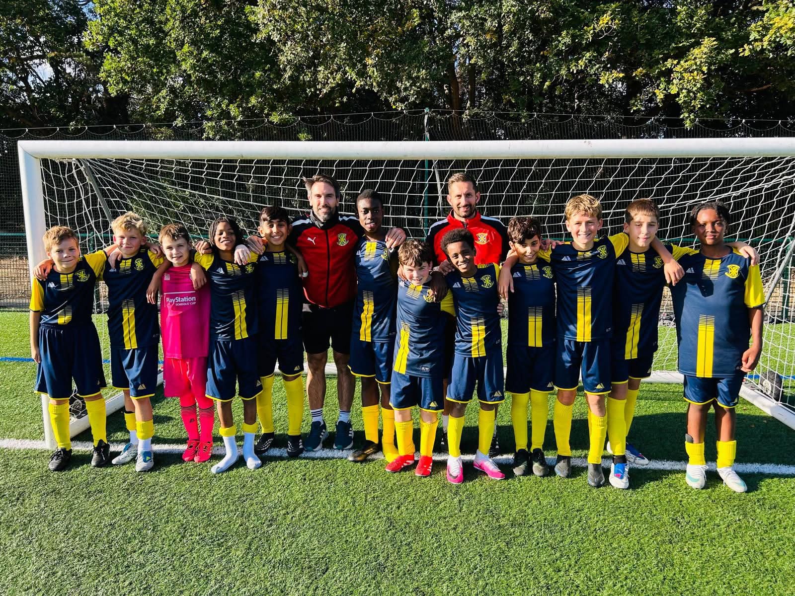 St. John’s Senior School football squad with their two coaches in a team photo on a sunny grass pitch