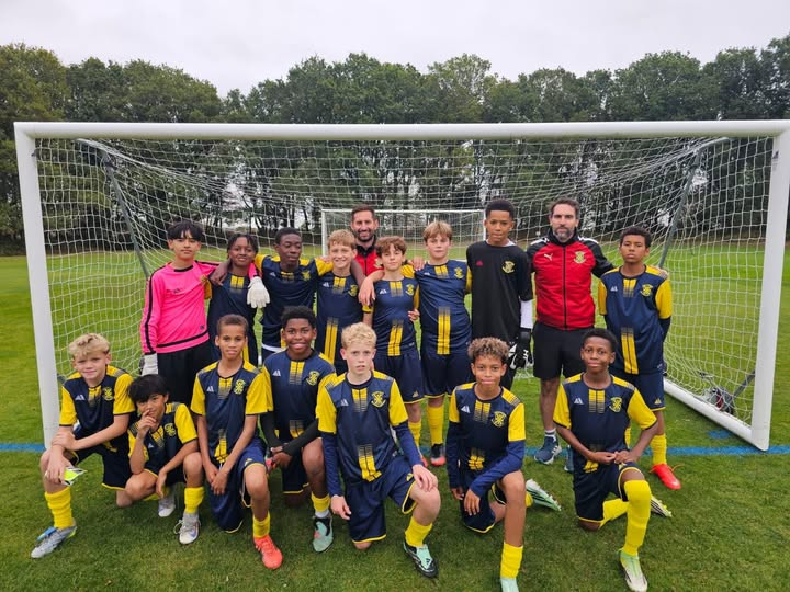 St. John’s football team posing in front of a goal on a grass pitch, with the front row kneeling and two coaches behind
